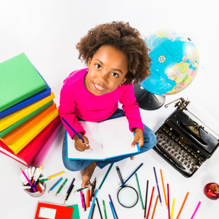 Élève écrivant dans un cahier, entourée de livres et de crayons de couleur